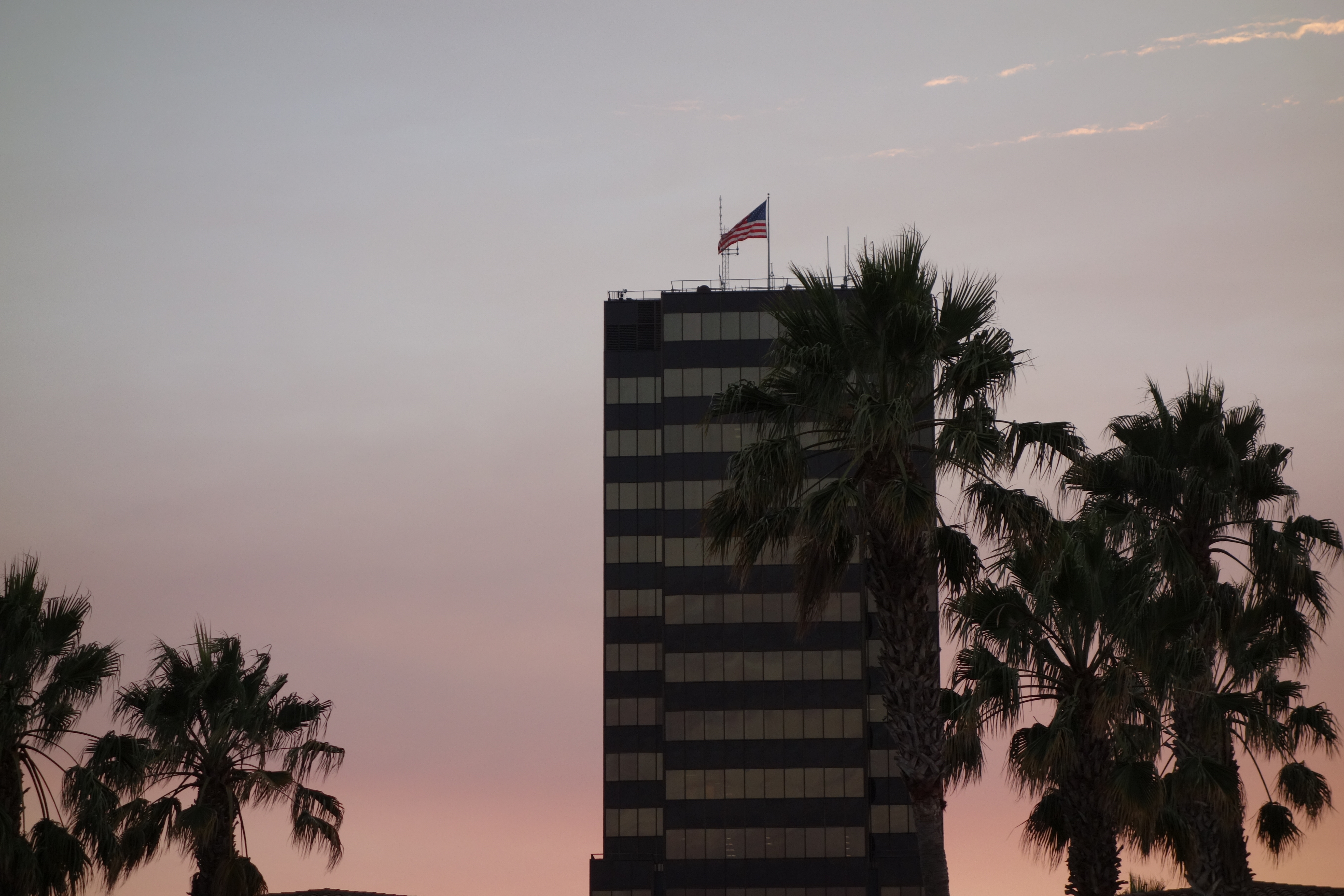 Sonnenuntergang im Hintergrund, im Vordergrund ein Hochhaus mit der amerikanischen Flagge