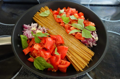 Spaghetti und Tomaten und Zwiebeln und Basilikum in einer Pfanne